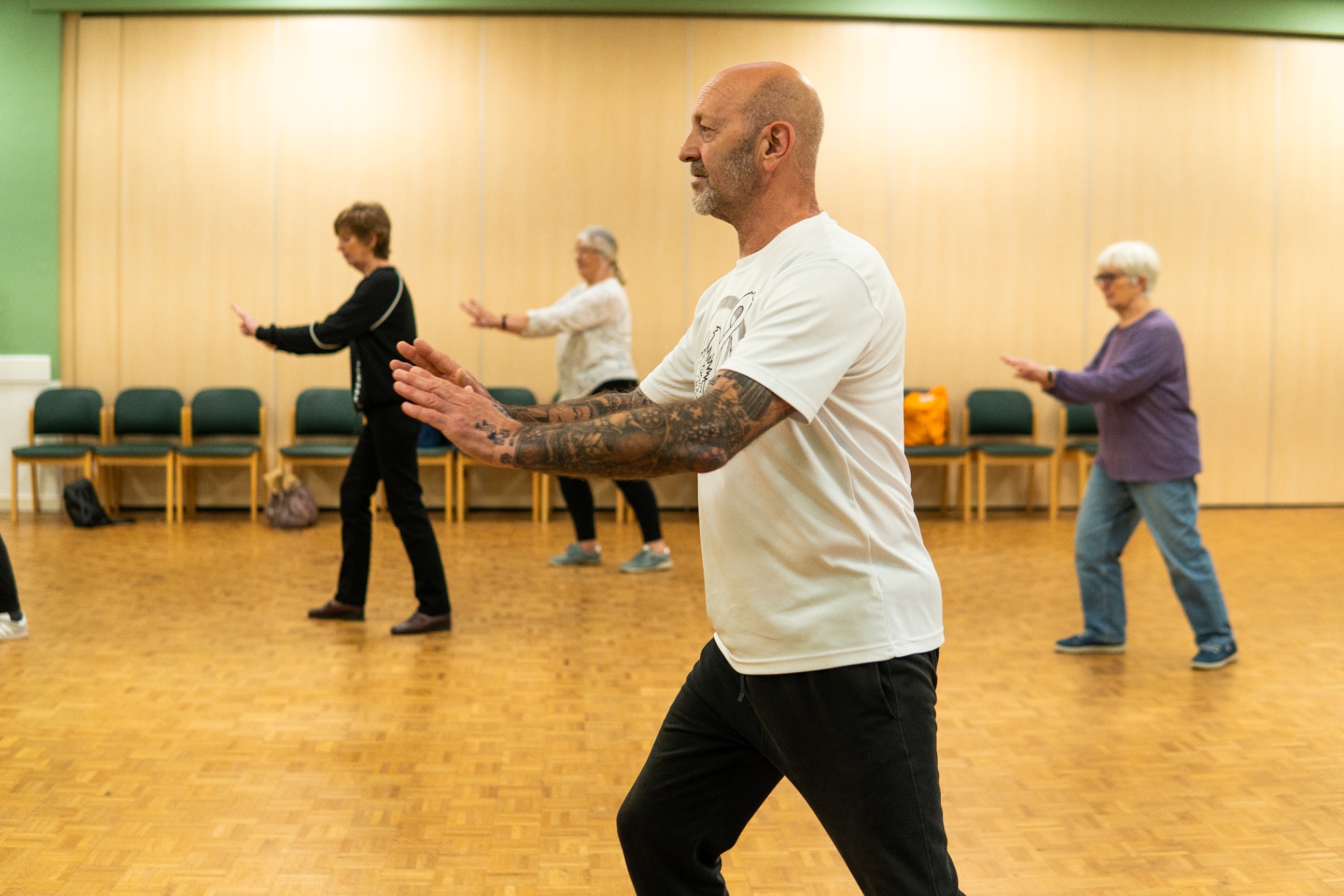 An older adult taking part in a gentle, guided exercise class, moving safely and with support.